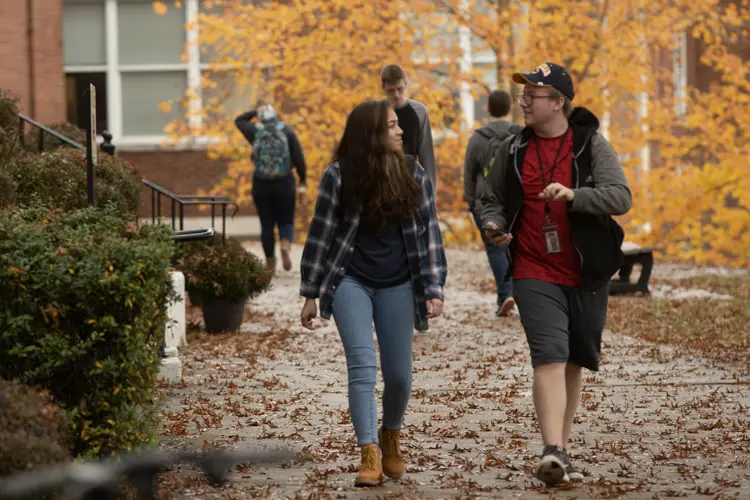 two students walking on campus surrounded by fall leaves